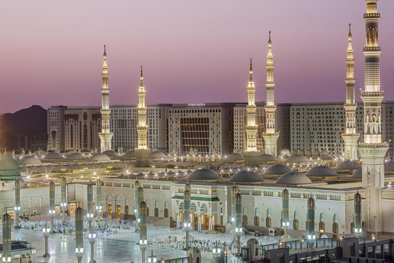 Hotel Intercontinental Dar Al Iman Madinah By Ihg Medina Esterno foto The photo shows a view of an expansive mosque complex, featuring several tall minarets that are illuminated against a twilight sky. The structure appears grand and is likely adorned with intricate architectural details. There are people gathered in t