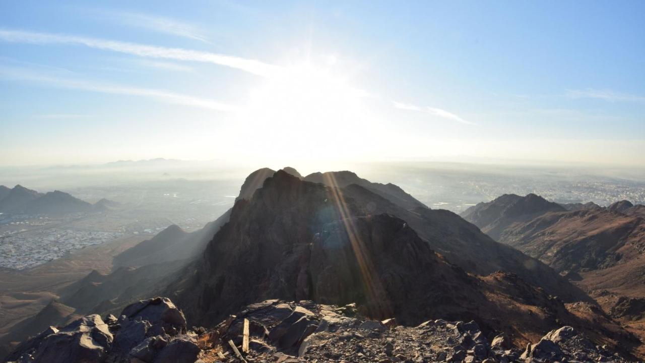 Hotel Intercontinental Dar Al Iman Madinah By Ihg Medina Esterno foto The photo shows a scenic view from a mountain top, with peaks silhouetted against the bright sun. The sun is positioned low in the sky, creating a warm glow and illuminating the landscape below. In the foreground, there are rocky terrains, while the 
