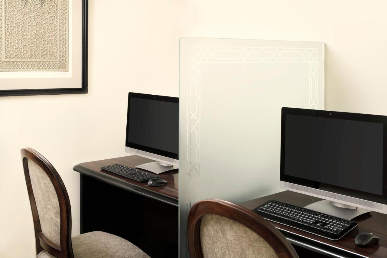 Hotel Intercontinental Dar Al Iman Madinah By Ihg Medina Esterno foto The photo shows a workspace featuring two computers set up on a dark wooden desk. Each computer has a monitor and a keyboard. A frosted glass partition is placed between the two workstations, providing some privacy. In the background, there is a fram