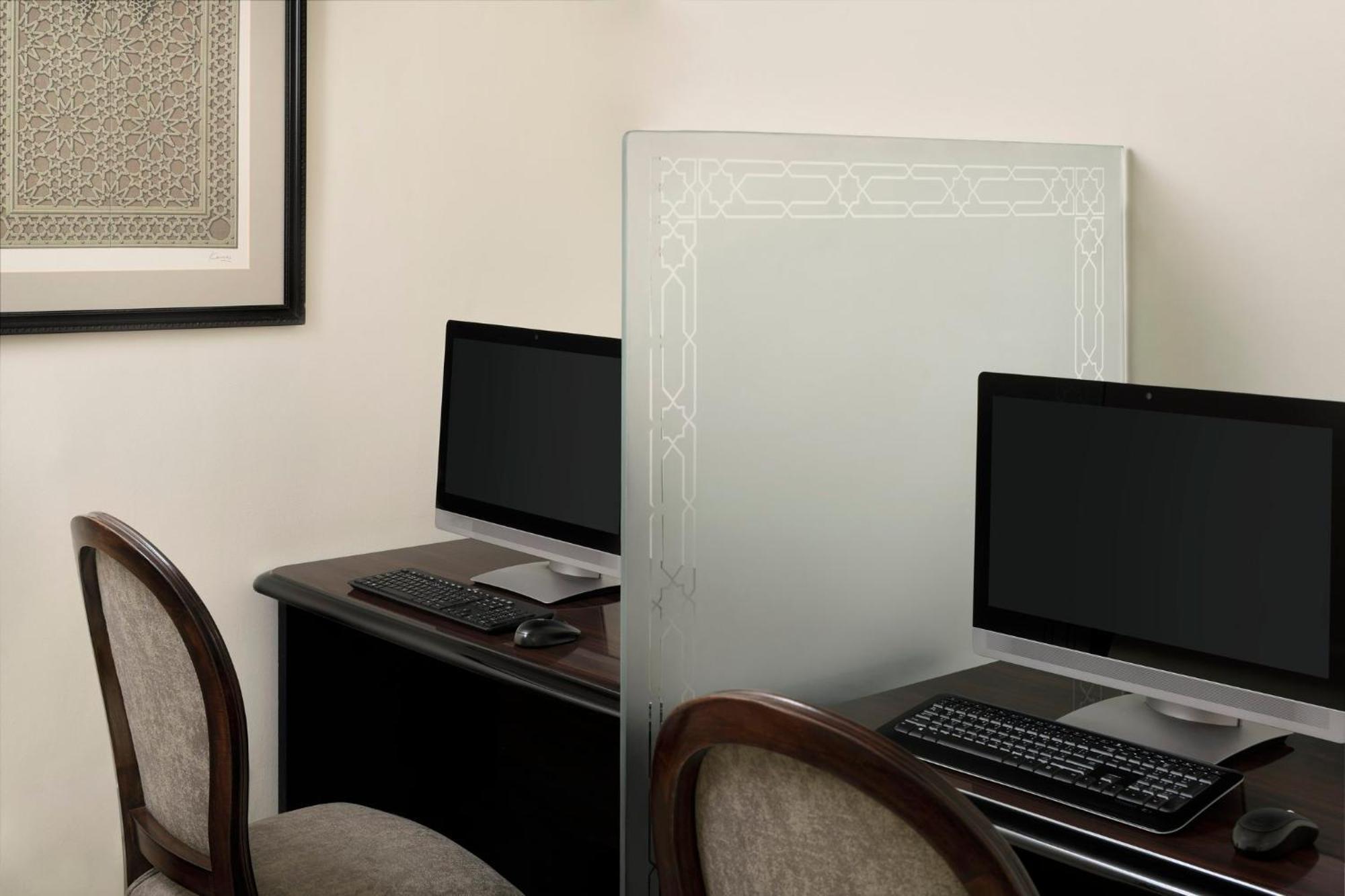 Hotel Intercontinental Dar Al Iman Madinah By Ihg Medina Esterno foto The photo shows a small office or workspace area featuring two computer stations. Each station has a black monitor, a keyboard, and appears to be set up on a dark wooden desk. A translucent glass partition is placed between the two workstations, prov