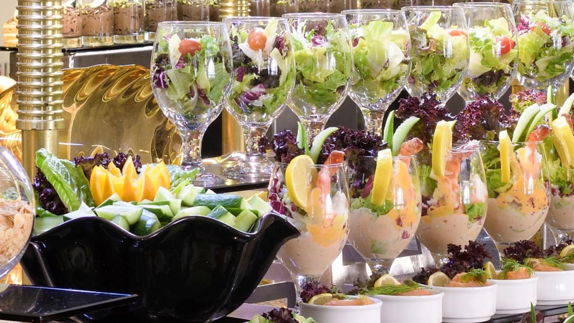 Hotel Intercontinental Dar Al Iman Madinah By Ihg Medina Esterno foto The photo features an elegant display of food items. In the background, there are several clear glasses filled with vibrant salads, featuring various types of greens and garnishes. In the foreground, there is a decorative black bowl containing cut pi