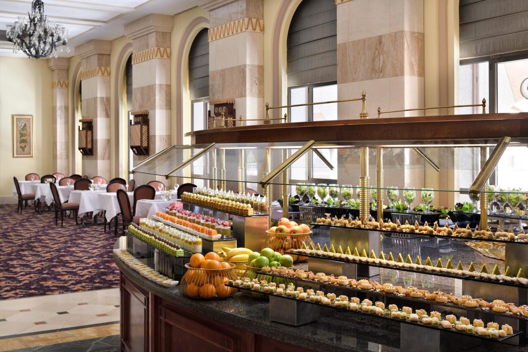Hotel Intercontinental Dar Al Iman Madinah By Ihg Medina Esterno foto The photo depicts an elegant dining area featuring a buffet-style display. In the foreground, a beautifully arranged buffet counter showcases an array of desserts, including miniature pastries and colorful fruit. The setting has a sophisticated ambia