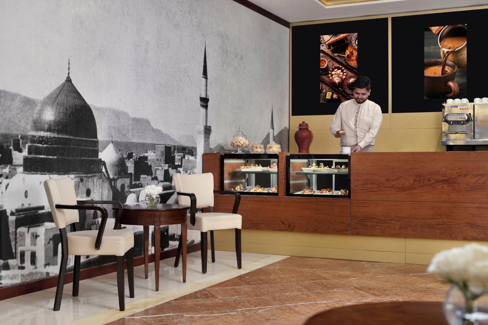 Hotel Intercontinental Dar Al Iman Madinah By Ihg Medina Esterno foto The photo shows a stylish interior of a café or pastry shop. In the background, there is a large black-and-white mural depicting a cityscape, featuring a prominent dome and minaret, suggesting an architectural style that could be from a Middle Easter