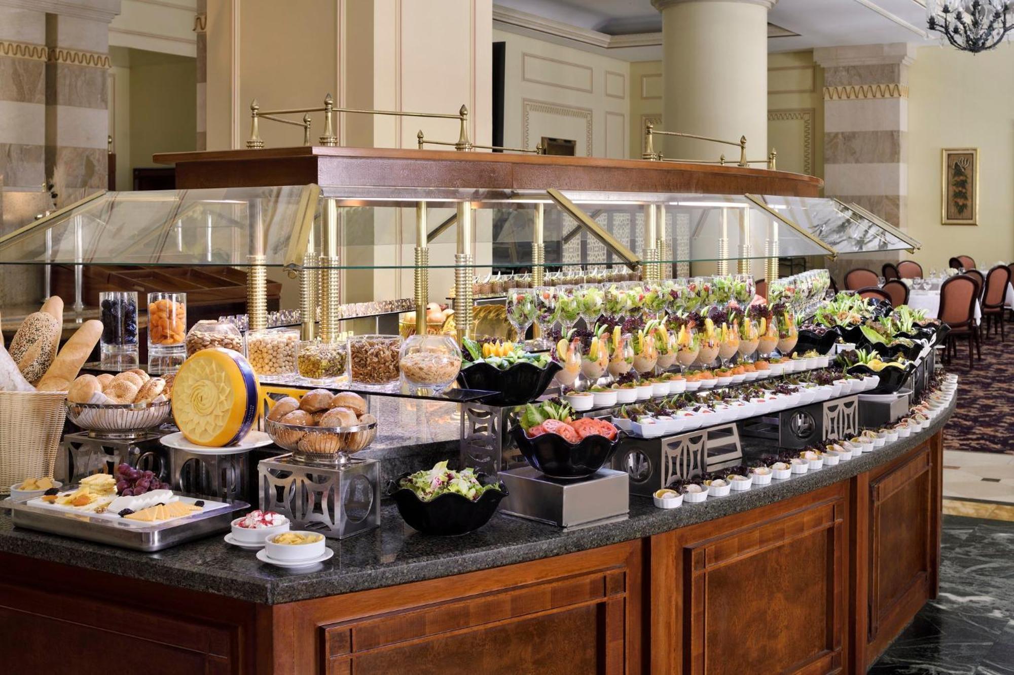 Hotel Intercontinental Dar Al Iman Madinah By Ihg Medina Esterno foto The photo shows an elegantly arranged buffet with a variety of food items. There is a large, curved wooden display with glass covers, showcasing an assortment of dishes. These include different types of breads and rolls, salads, garnishes, and desser