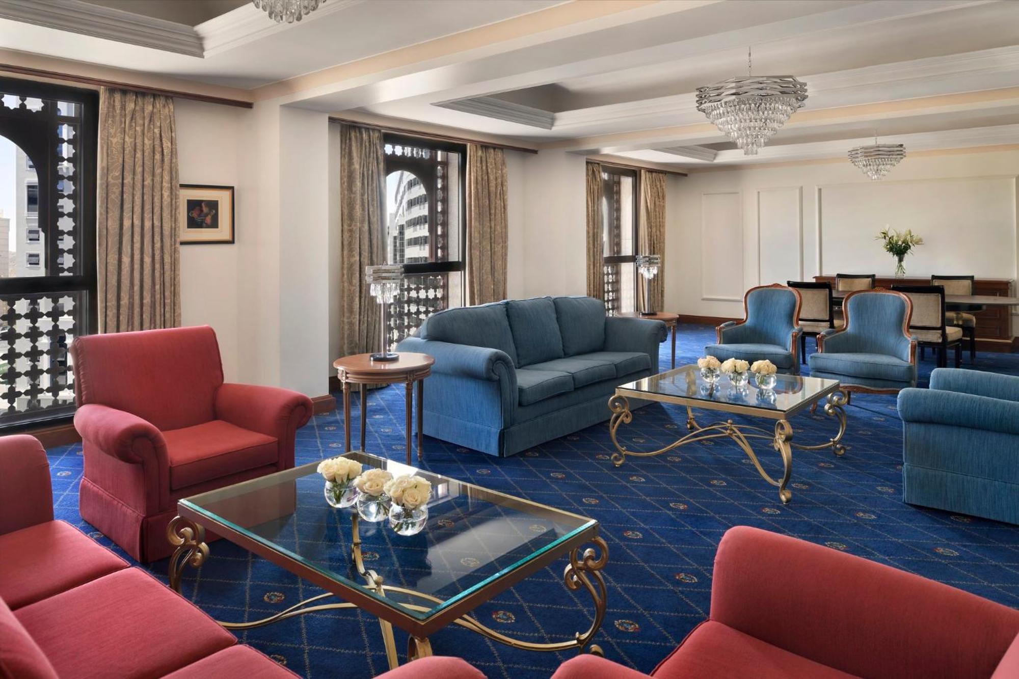 Hotel Intercontinental Dar Al Iman Madinah By Ihg Medina Esterno foto The photo shows a luxurious living space or lounge area. It features a combination of furniture, including a blue sofa, several red armchairs, and glass-top coffee tables with gold accents. The flooring is carpeted in a deep blue, and the walls are a