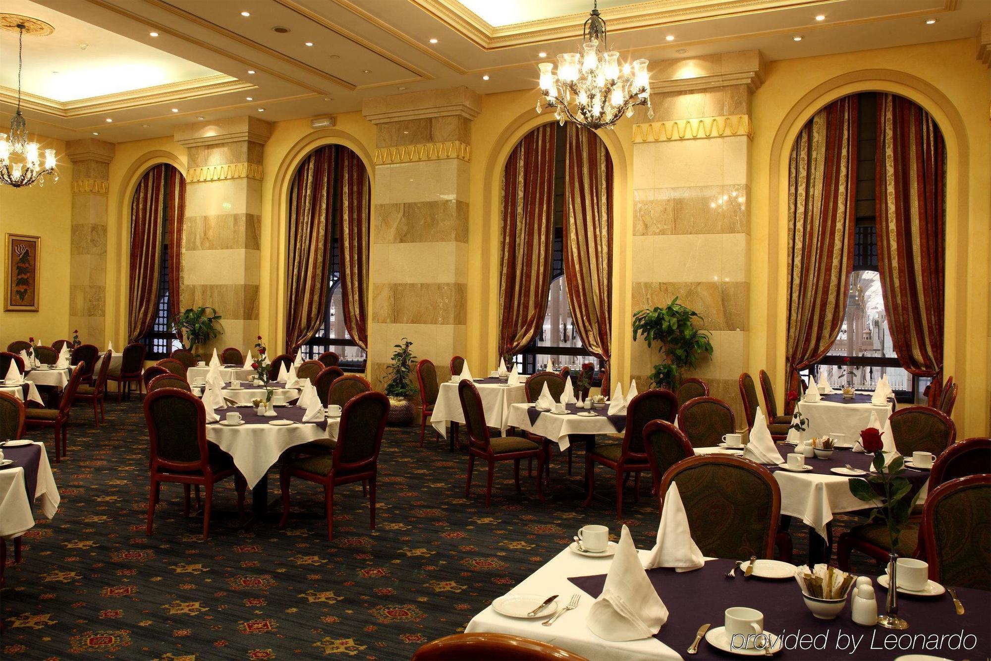 Hotel Intercontinental Dar Al Iman Madinah By Ihg Medina Ristorante foto The photo depicts an elegant restaurant interior. The space features ornate decor with tall windows draped in rich, patterned curtains. Tables are neatly set with white tablecloths and napkins, and there are plush chairs arranged around them. The flo