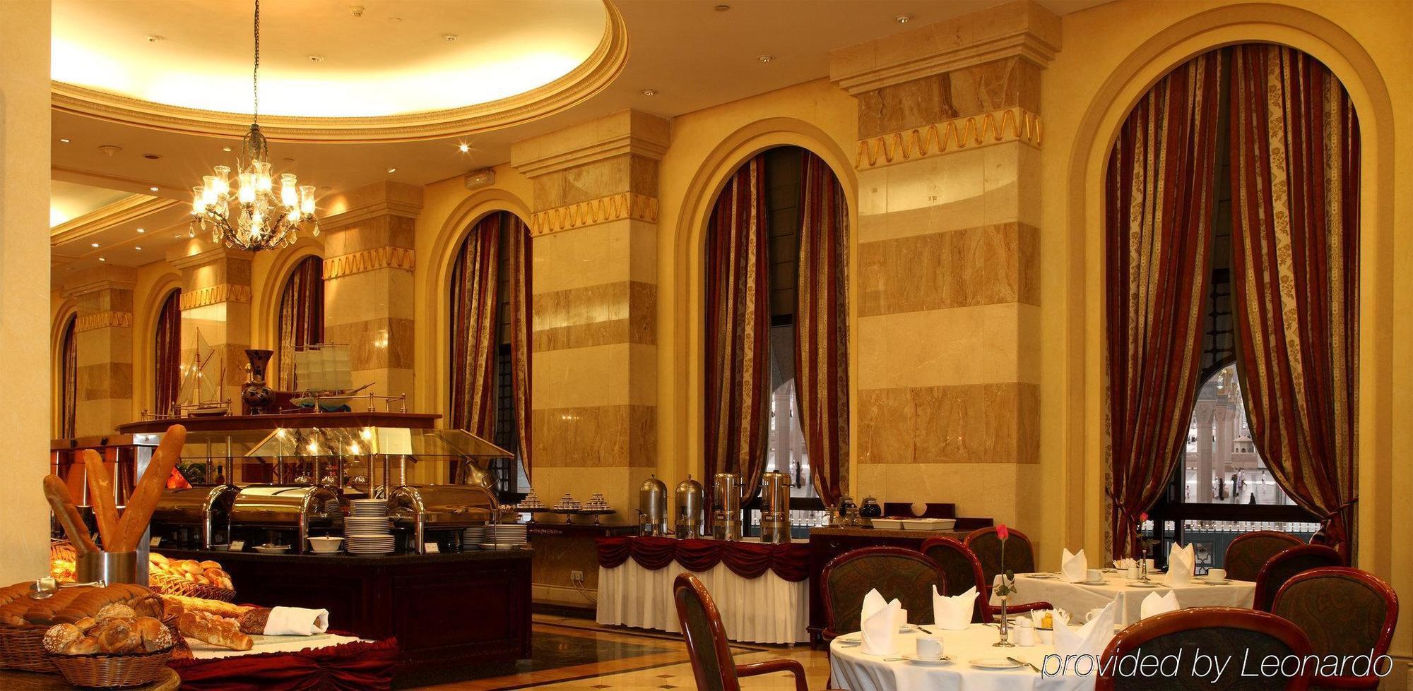 Hotel Intercontinental Dar Al Iman Madinah By Ihg Medina Ristorante foto The photo shows an elegant dining restaurant interior. It features stylish arches and walls with a blend of marble and decorative elements. There are large windows draped with rich curtains, contributing to the luxurious atmosphere. The dining area i