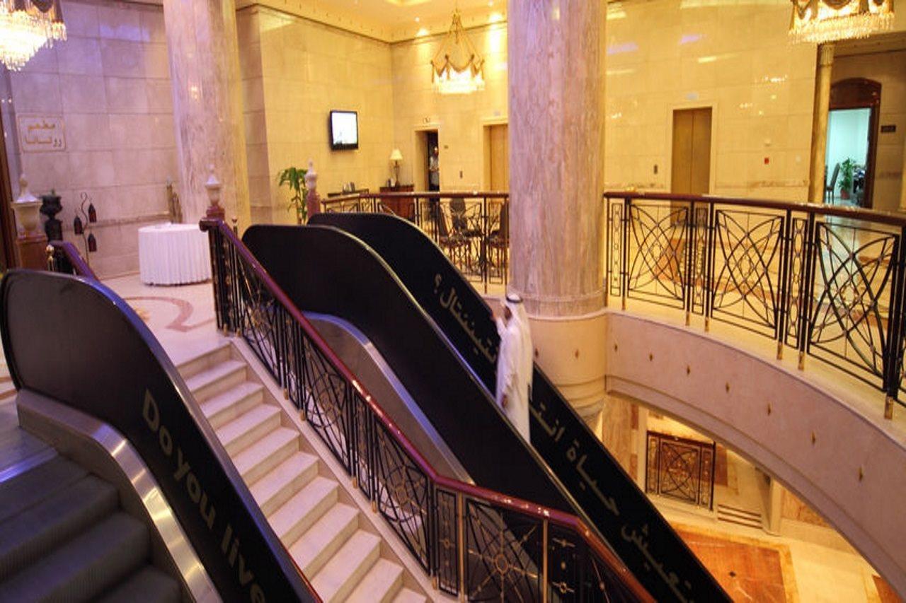 Hotel Intercontinental Dar Al Iman Madinah By Ihg Medina Interno foto The photo depicts an elegant interior space, likely within a hotel or a large building. There is a grand staircase visible, which features a combination of stairs and escalators. The design includes decorative railings and marble pillars, contributin
